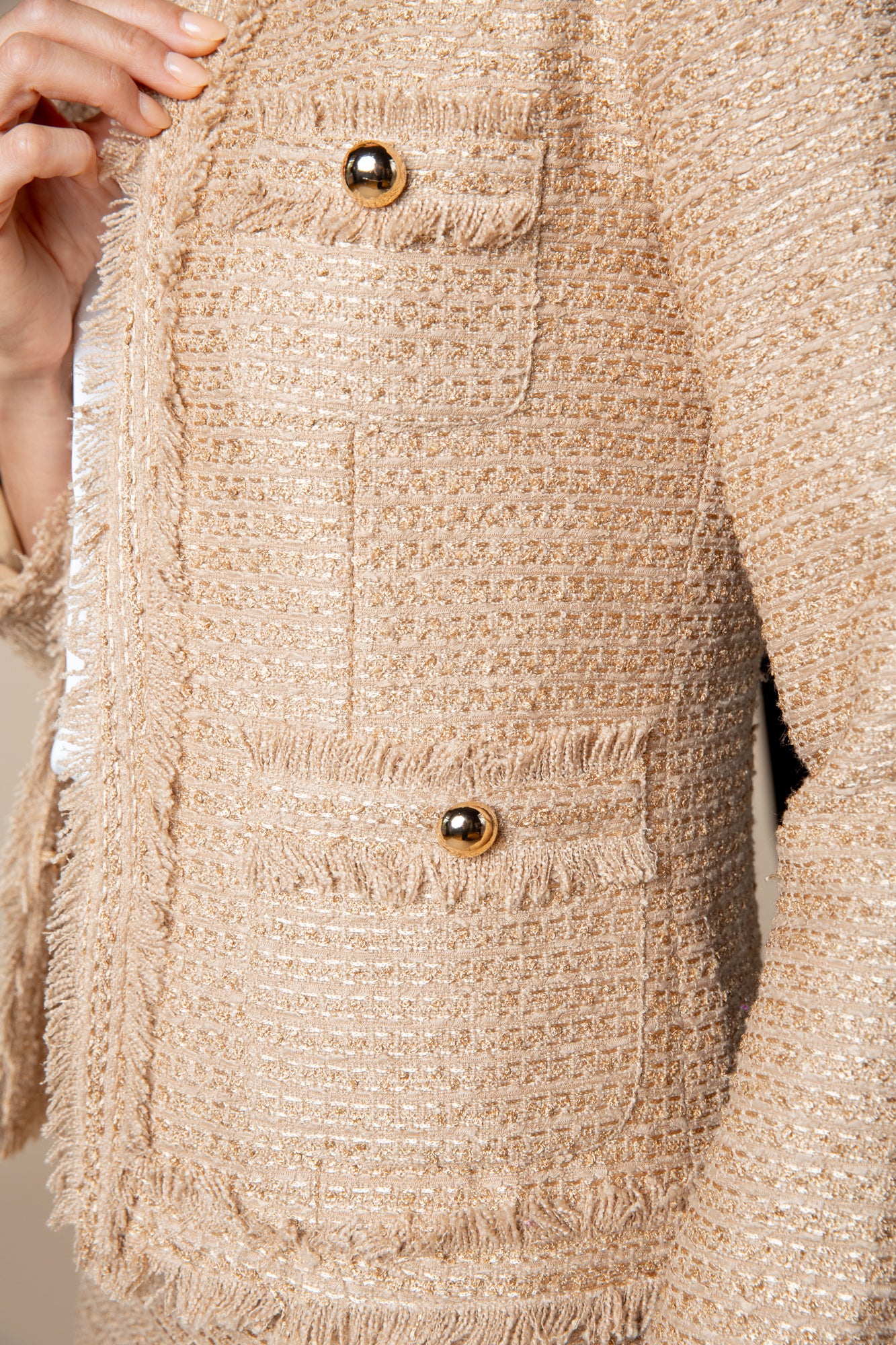 Detailfoto: Beige Jacke "Honey Glow" mit edlem Goldschimmer, goldfarbenen Knöpfen und handgemachten, doppelt ausgefransten Enden. 